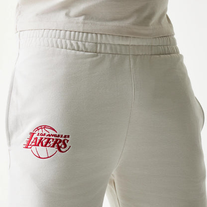 New Era LA Lakers NBA League Essential Cream Shorts, three-quarter view showing the elastic waistband and an embroidered red Lakers logo on the left thigh, worn with a matching cream top.