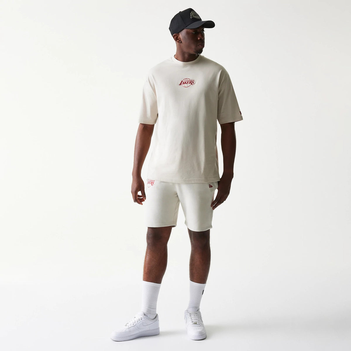 New Era LA Lakers NBA League Essential Cream Shorts, on-model view showing cream shorts with an embroidered Lakers logo on the left leg, paired with a matching cream T-shirt featuring the same logo centrally on the chest.