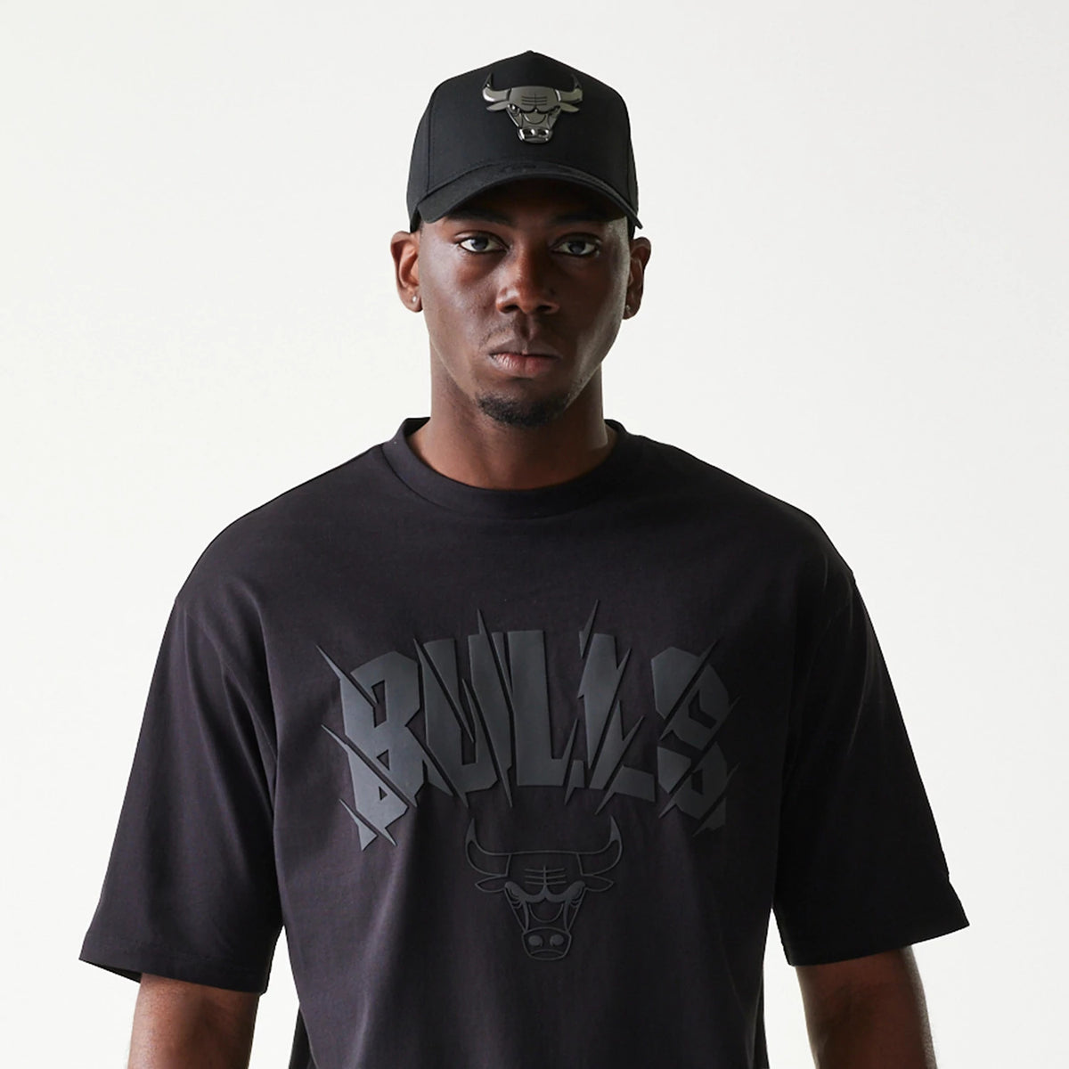 New Era Chicago Bulls NBA Black Oversized T-Shirt, front view on-model showing a large Bulls graphic on the chest, styled with a matching black cap featuring an embroidered Bulls logo on the front.