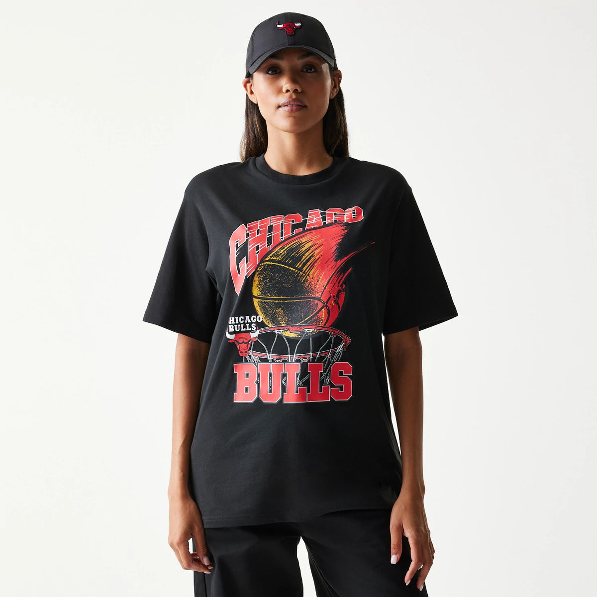 New Era Chicago Bulls NBA Ball Graphic Black T-Shirt, front view on-model featuring a basketball graphic with a flaming ball above a hoop, large Chicago Bulls lettering, and the model styled with a matching cap.