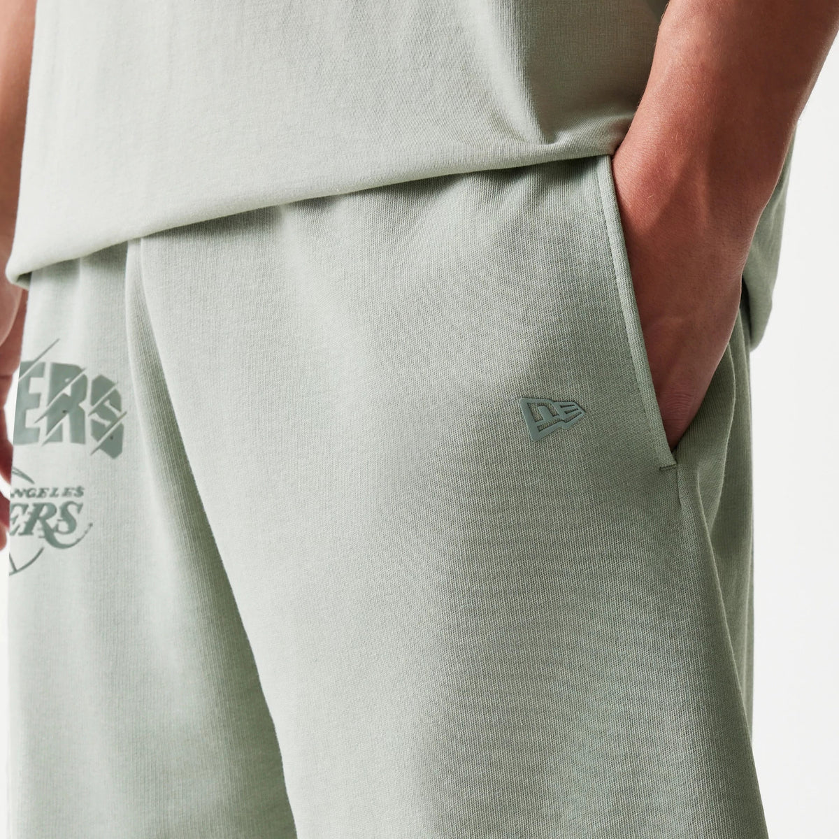 New Era LA Lakers NBA Pastel Green Shorts, front view showing the pastel green fabric with an embroidered New Era logo near the side pocket and the Los Angeles Lakers graphic in stylised lettering on the thigh.