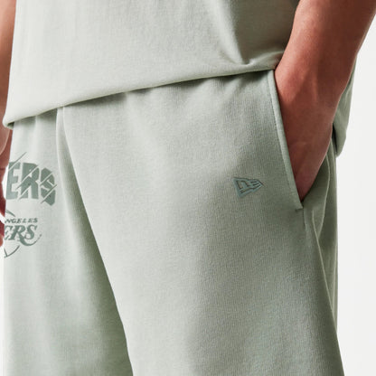 New Era LA Lakers NBA Pastel Green Shorts, front view showing the pastel green fabric with an embroidered New Era logo near the side pocket and the Los Angeles Lakers graphic in stylised lettering on the thigh.