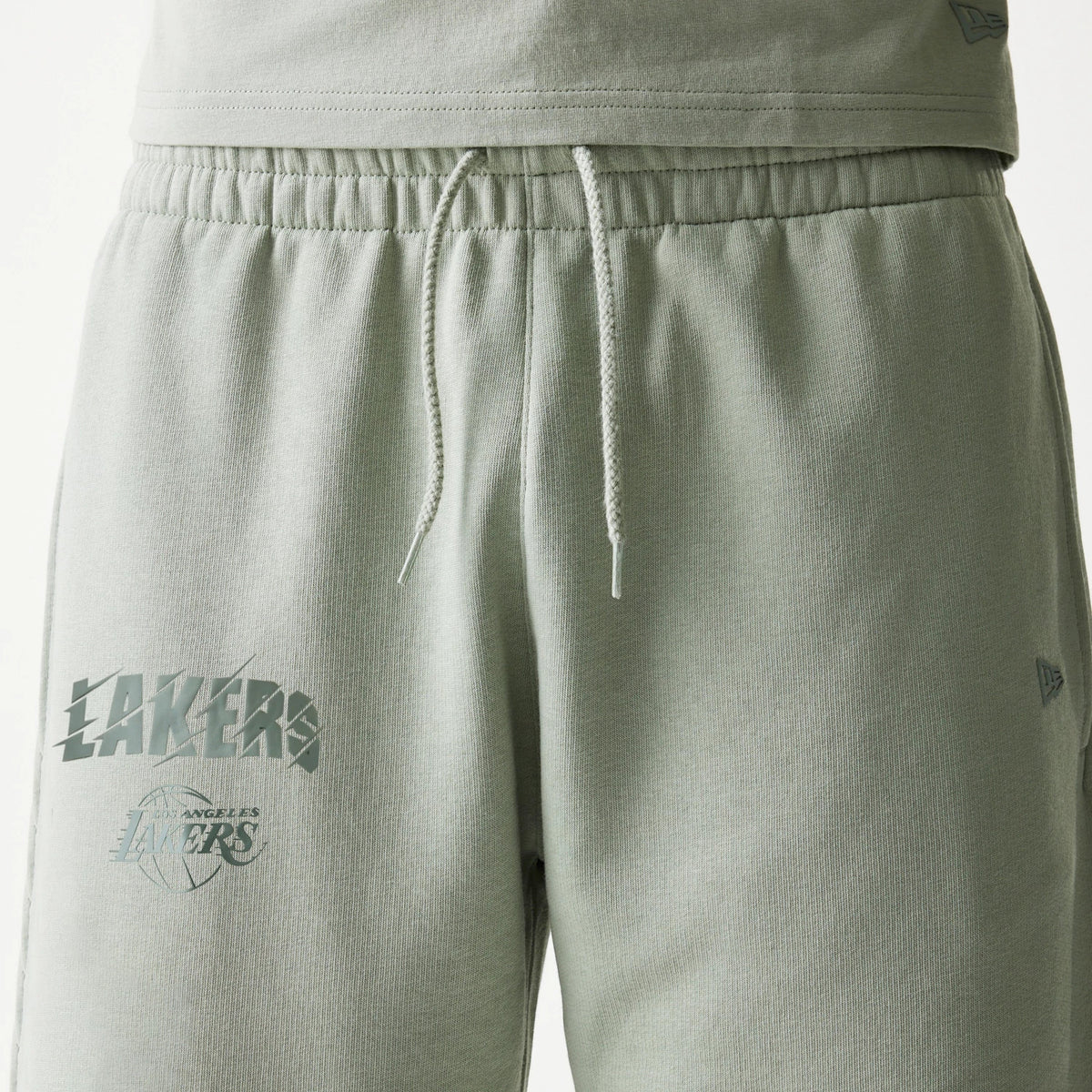 New Era LA Lakers NBA Pastel Green Shorts, front view showing a drawstring waistband and two printed Lakers logos on the left thigh with a small embroidered New Era logo above the hem on the right leg.