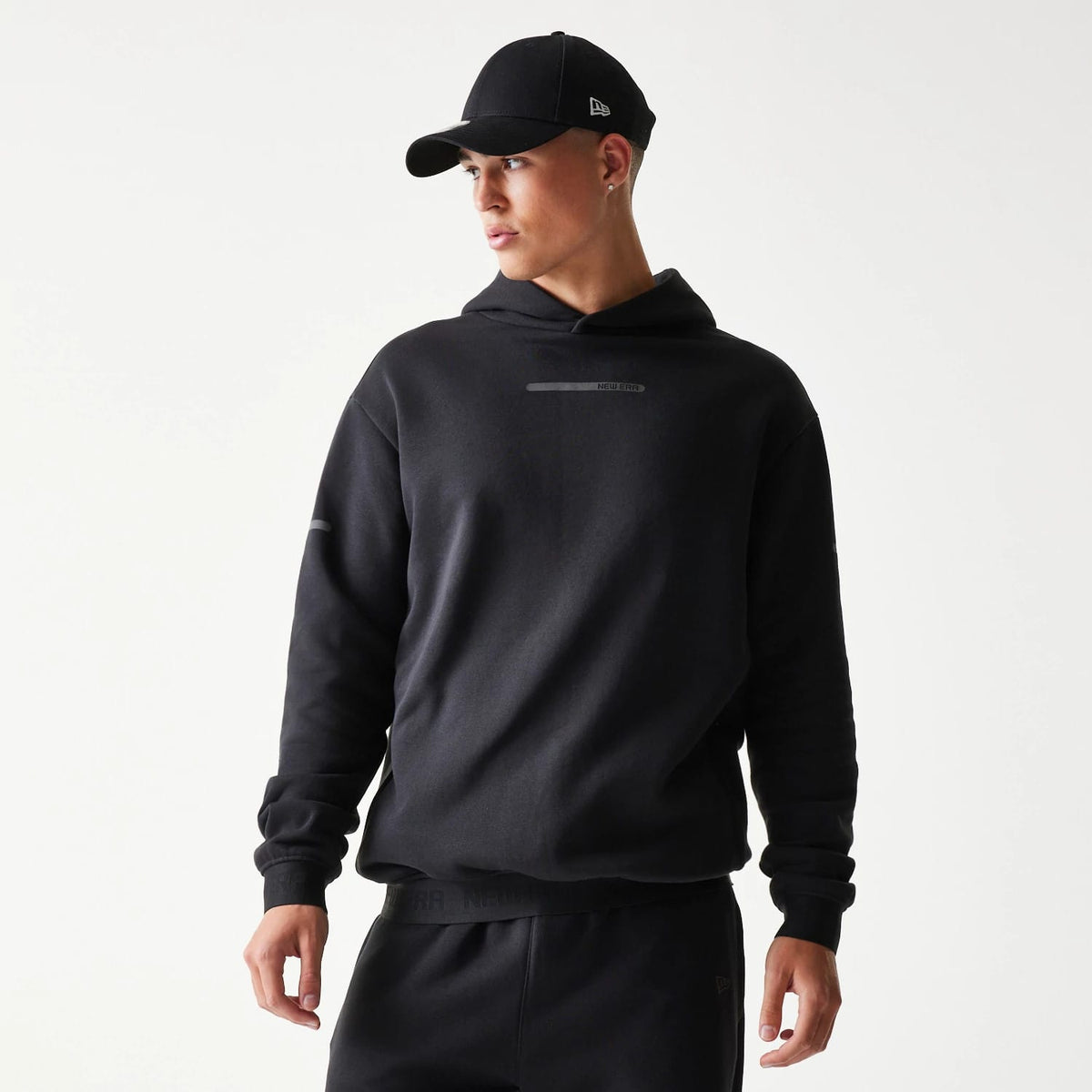 The model is wearing this New Era Tech Strip Oversized Pullover Hoodie in black. 3