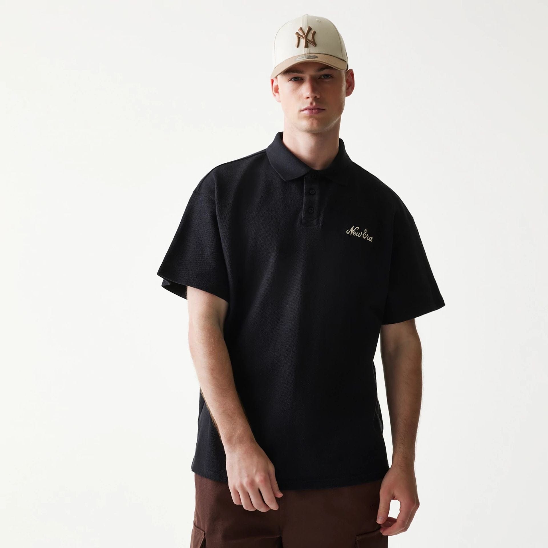 The model is wearing this New Era Graphic Polo T-Shirt in black. 1