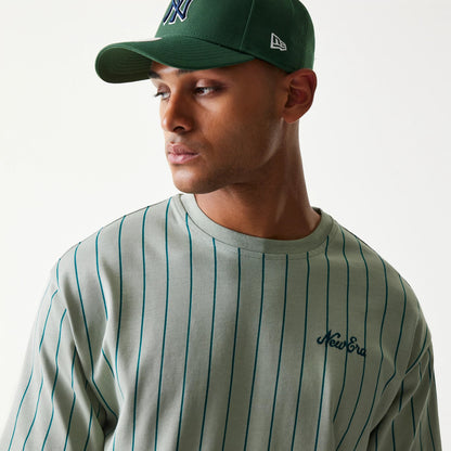 New Era Pinstripe Pastel Green Oversized T-Shirt, on-model front view showing vertical dark green pinstripes on the pastel green fabric and an embroidered New Era logo on the left chest, styled with a matching green cap.
