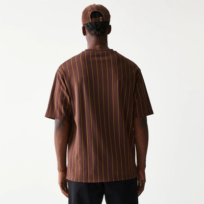 New Era Pinstripe Brown Oversized T-Shirt, back view on a model showing vertical yellow pinstripes on the brown fabric and a relaxed fit, paired with a brown cap that features an adjustable strap at the back.