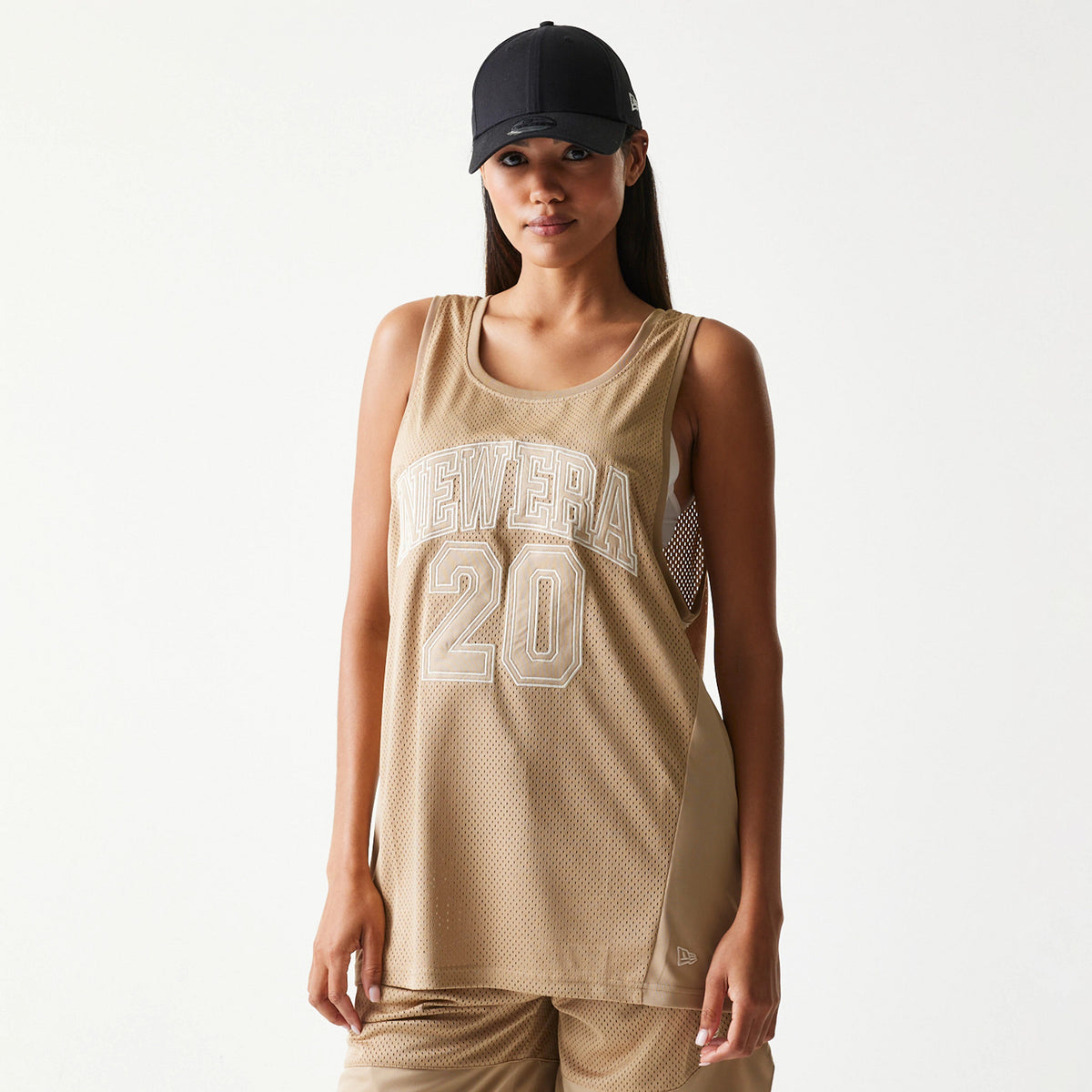 New Era Mesh Light Beige Tank Top, front view on a model with a black cap, featuring white outlined New Era lettering and number 20 embroidered on the chest over a light beige mesh fabric.