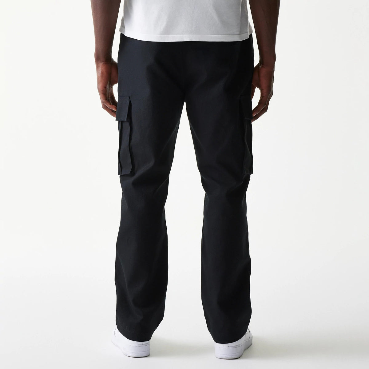 New Era Black Straight Leg Cargo Joggers, rear view on a model showing the relaxed fit and dual large flap pockets on the sides, the hem resting on white trainers.