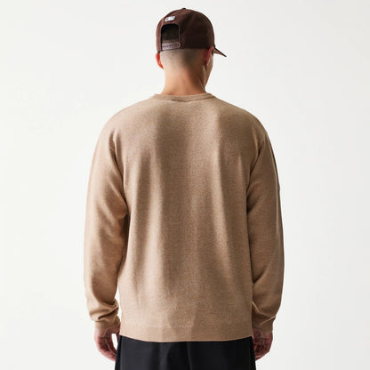 New Era Essential Flag Light Beige Knitted Sweater, back view on a model wearing a dark cap, showing the light beige texture of the sweater with ribbed cuffs and hem, offering a relaxed fit over dark trousers.