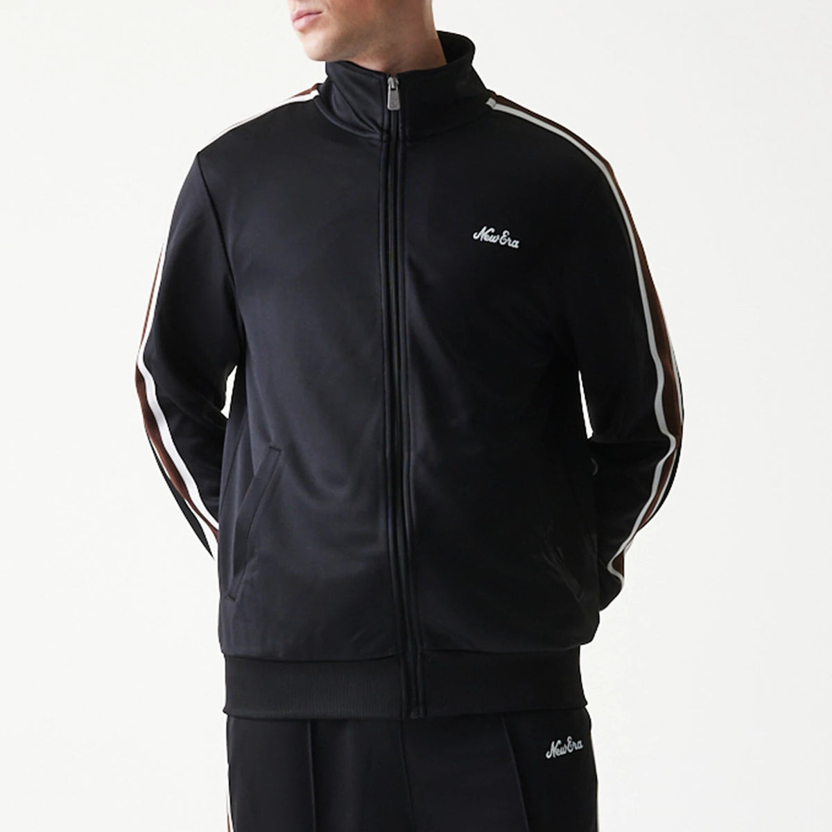 New Era Script Black Track Jacket, front view on-model showing the black jacket with a white embroidered New Era logo on the left chest, full zip closure, and white side stripes running down the length of the sleeves.