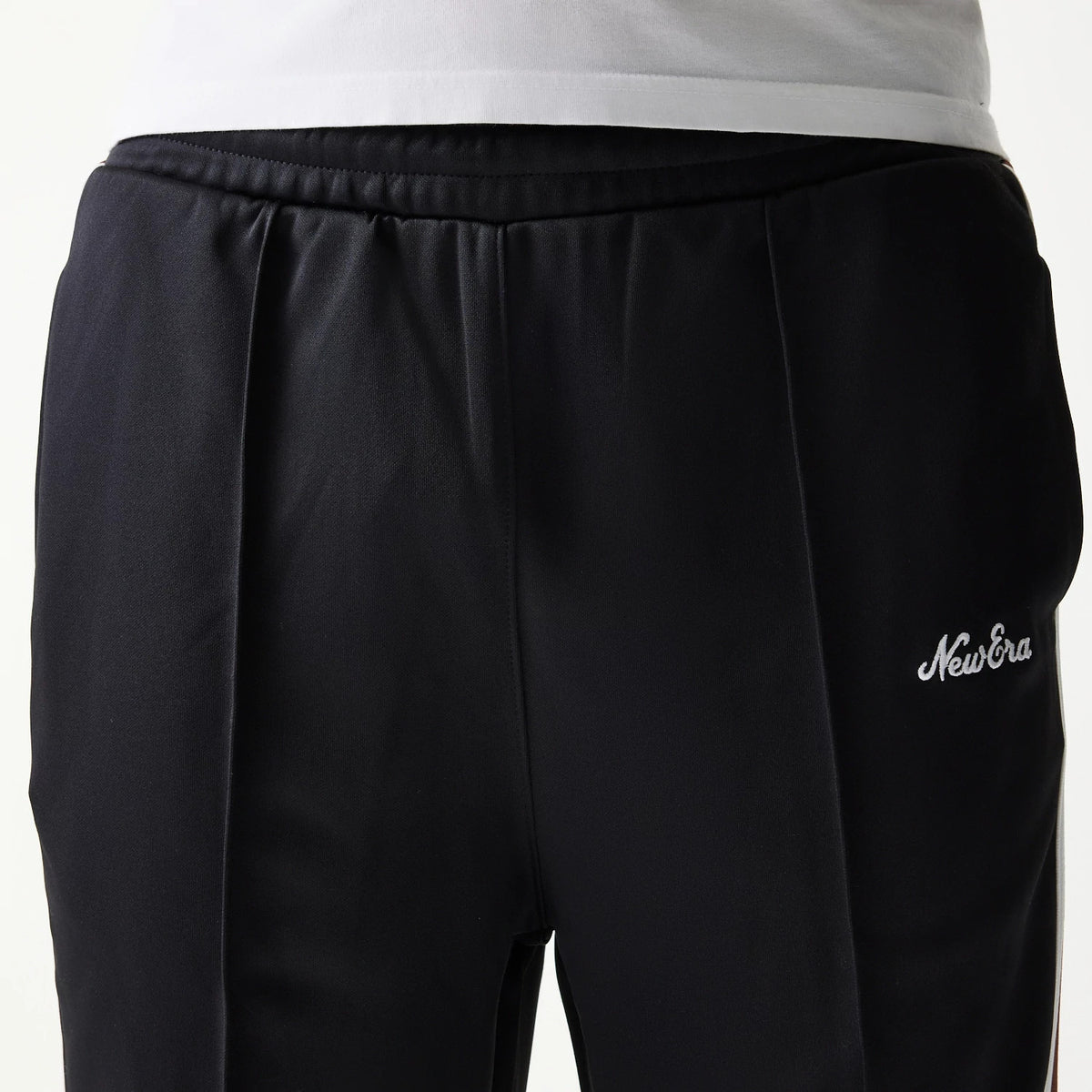 New Era Script Black Straight Leg Joggers, close-up view showing the white embroidered New Era script logo on the left side near the waist, with pleated on the black fabric and an elasticated waistband.