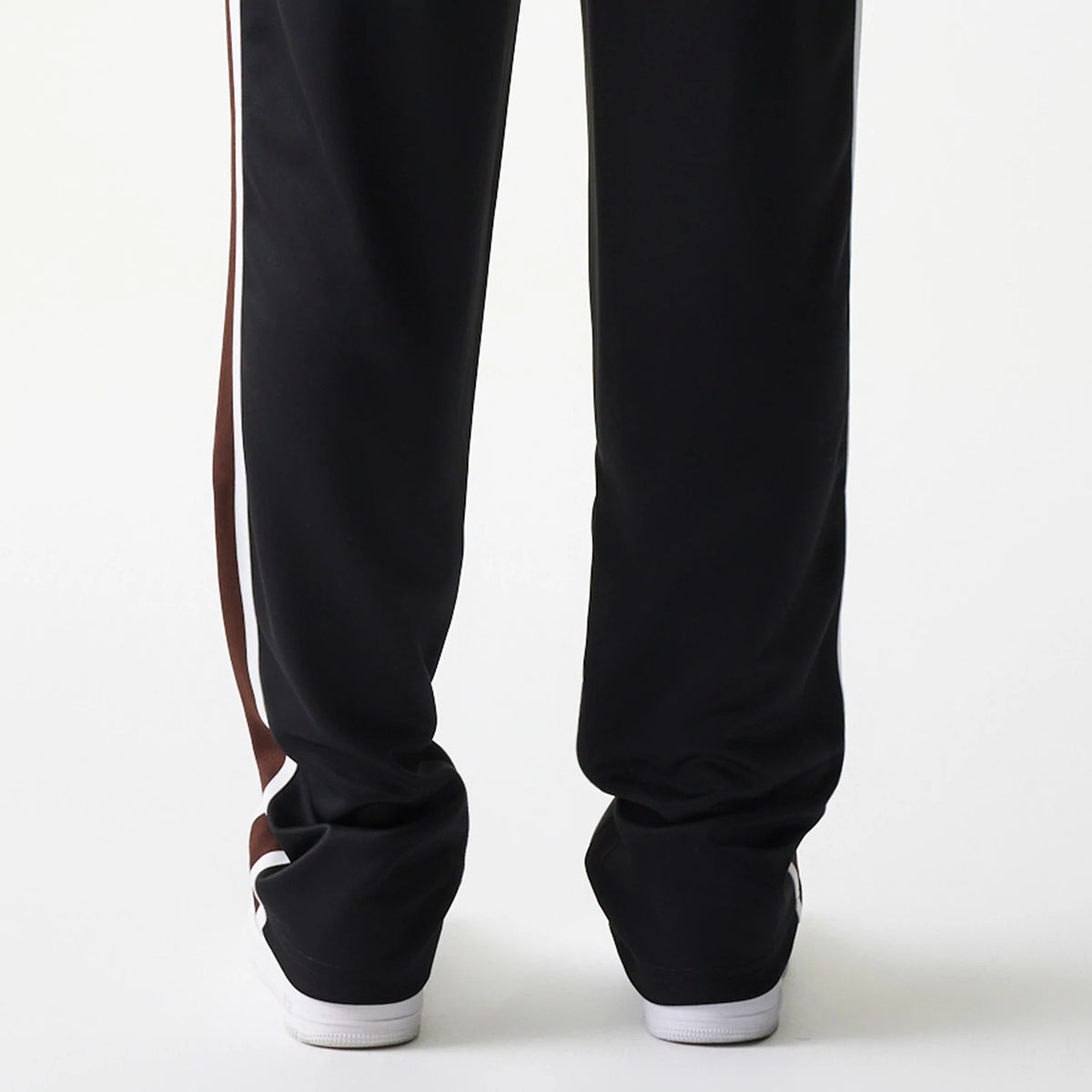 New Era Script Black Straight Leg Joggers, rear view showing a black fabric finish with contrasting white and brown side stripes, slightly relaxed fit at the ankles paired with white trainers.