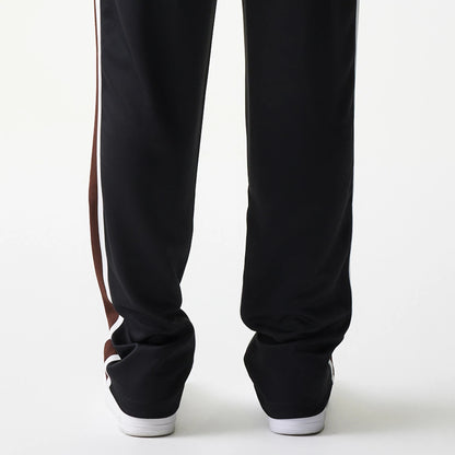 New Era Script Black Straight Leg Joggers, rear view showing a black fabric finish with contrasting white and brown side stripes, slightly relaxed fit at the ankles paired with white trainers.