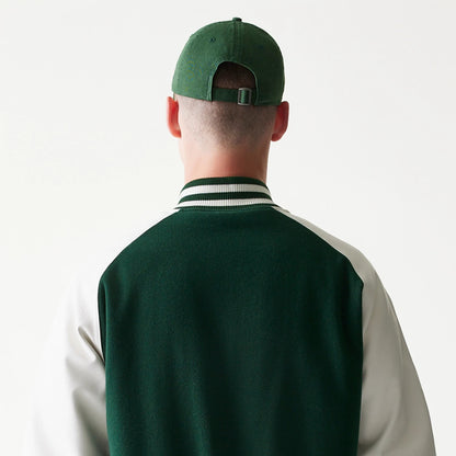 New Era LA Dodgers MLB Dark Green Varsity Jacket, back view on-model showing the dark green body with contrasting white sleeves, double-striped ribbed collar, and a dark green cap with eyelets worn by the model.