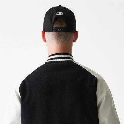 New Era New York Yankees MLB Black Varsity Jacket, back view on a model showing the black and white sleeve contrast, a stripe detail along the collar and a black cap with a white embroidered logo above.