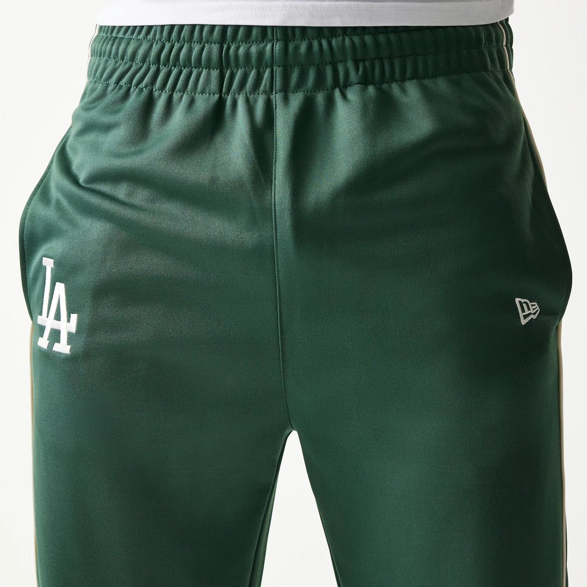 New Era LA Dodgers MLB Piping Dark Green Straight Leg Joggers, front view showing the white LA logo on the left thigh and the New Era flag logo on the right, with an elasticated waistband above a straight leg fit.