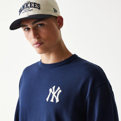 New Era New York Yankees MLB Essential Navy Knitted Sweater, on-model view showing the white embroidered Yankees logo on the chest, worn by a model also wearing a beige Yankees cap with navy visor and New Era flag logo on the side.