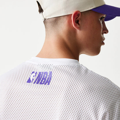 New Era LA Lakers NBA Graphic Mesh White T-Shirt, back view on-model showing the white mesh fabric with purple NBA lettering just below the neckline, paired with a beige and purple cap worn by the model.