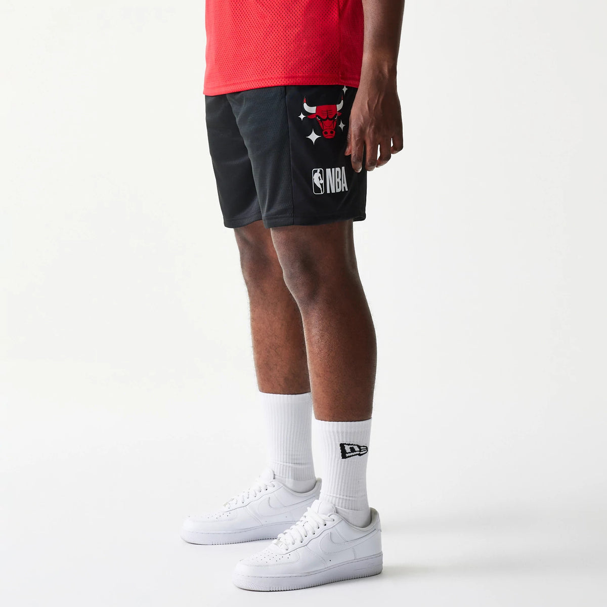New Era Chicago Bulls NBA Mesh Black Shorts, side view on a model with matching socks, featuring a red embroidered Bulls logo on the right thigh above a printed NBA logo, set against a solid black mesh fabric.