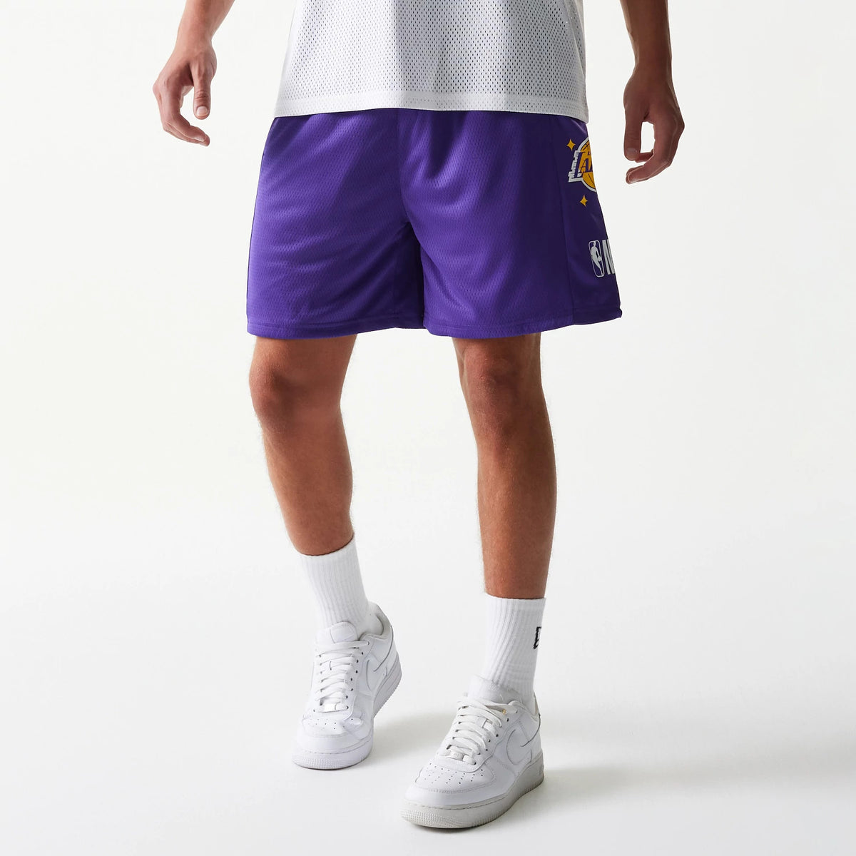 New Era LA Lakers NBA Mesh Purple Shorts, front view showing the embroidered Lakers logo on the left leg in yellow and white, set against the purple mesh fabric, worn with white socks and trainers.
