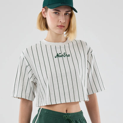 Womens New Era Pinstripe Pastel Grey Cropped T-shirt, front view on-model showing vertical dark green pinstripes on a grey background with an embroidered New Era logo at the centre of the chest, paired with matching green sports cap and trousers.