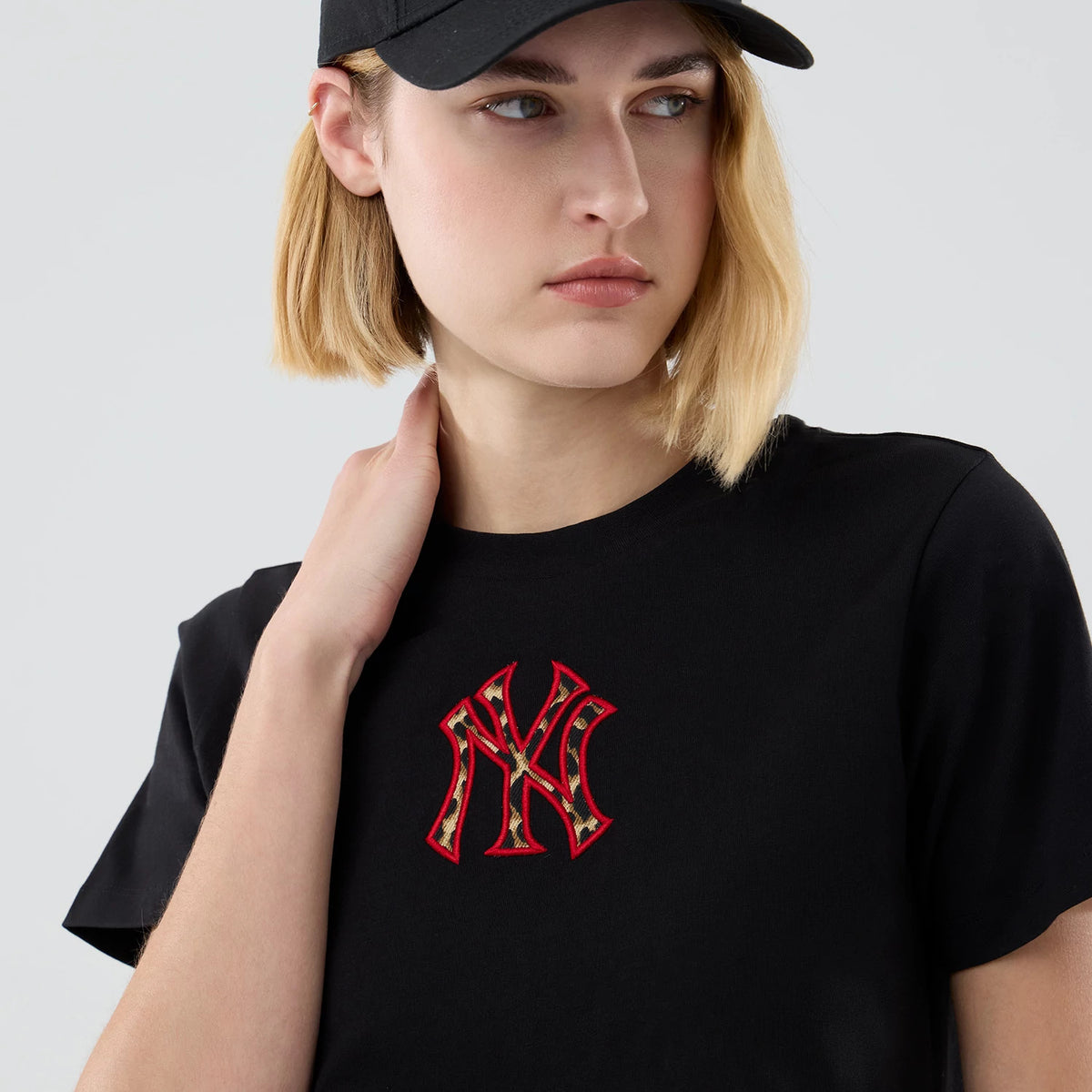 New Era New York Yankees Womens MLB Infill Black T-shirt, front view on a model showing a prominent red embroidered Yankees logo with patterned infill at the centre of the chest, paired with a plain black cap.