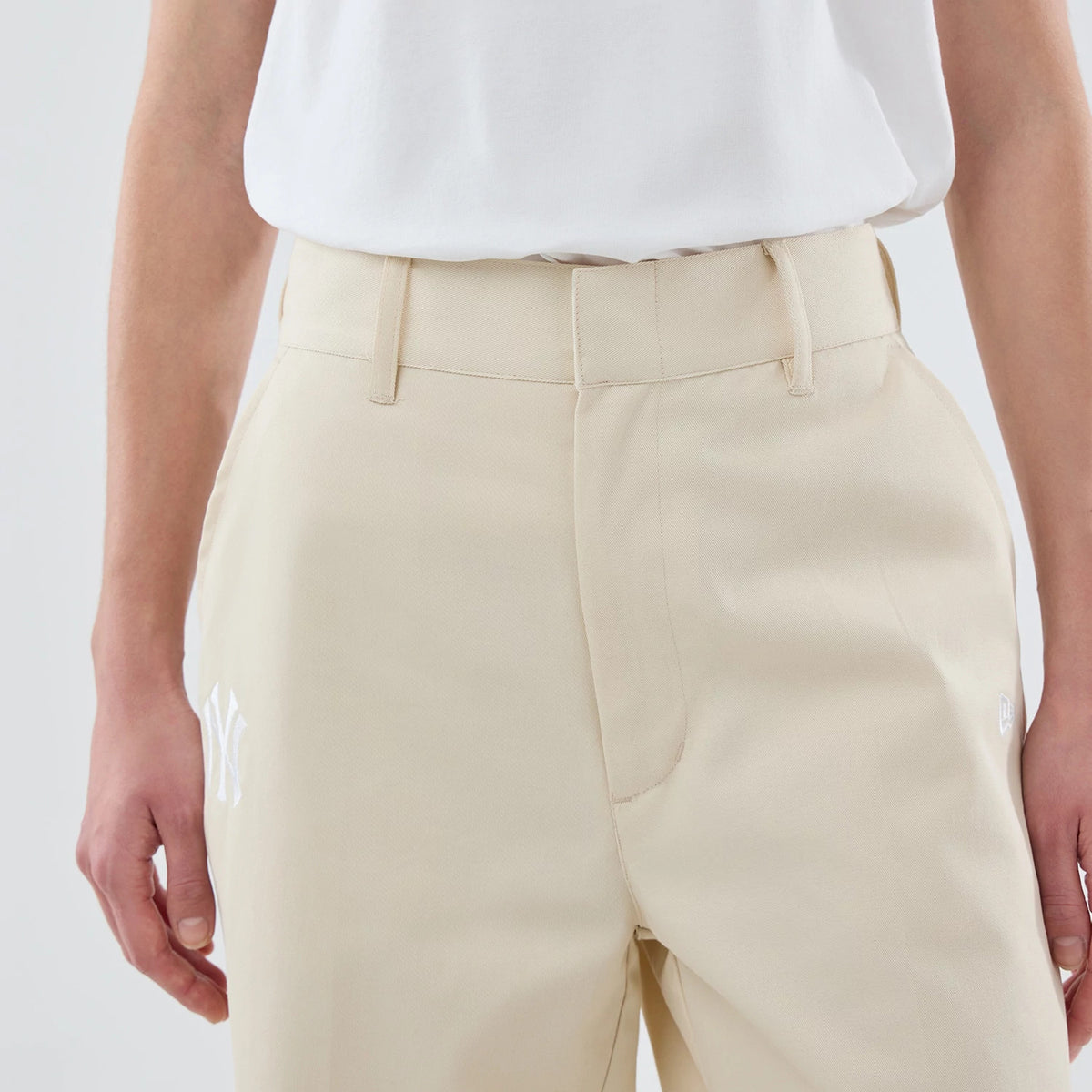 New Era New York Yankees Womens MLB Cream Chino Trousers, front view on a model wearing a plain white top, featuring white NY logo embroidery on the left thigh and neat belt loops on the waistband.