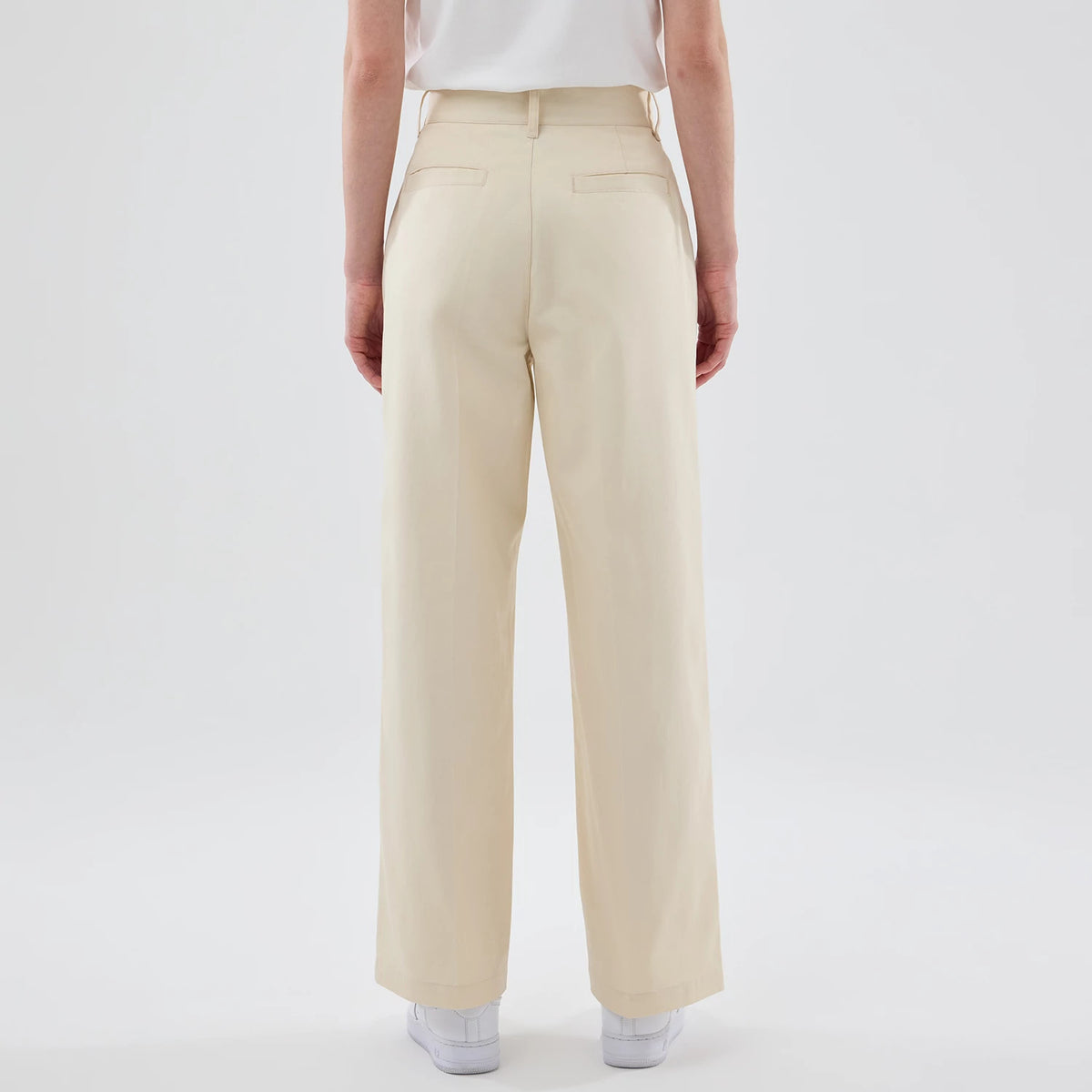New Era New York Yankees Womens MLB Cream Chino Trousers, rear view on a model highlighting the high-waisted design with belt loops, two welt pockets, and a straight-leg fit with hems falling over white trainers.