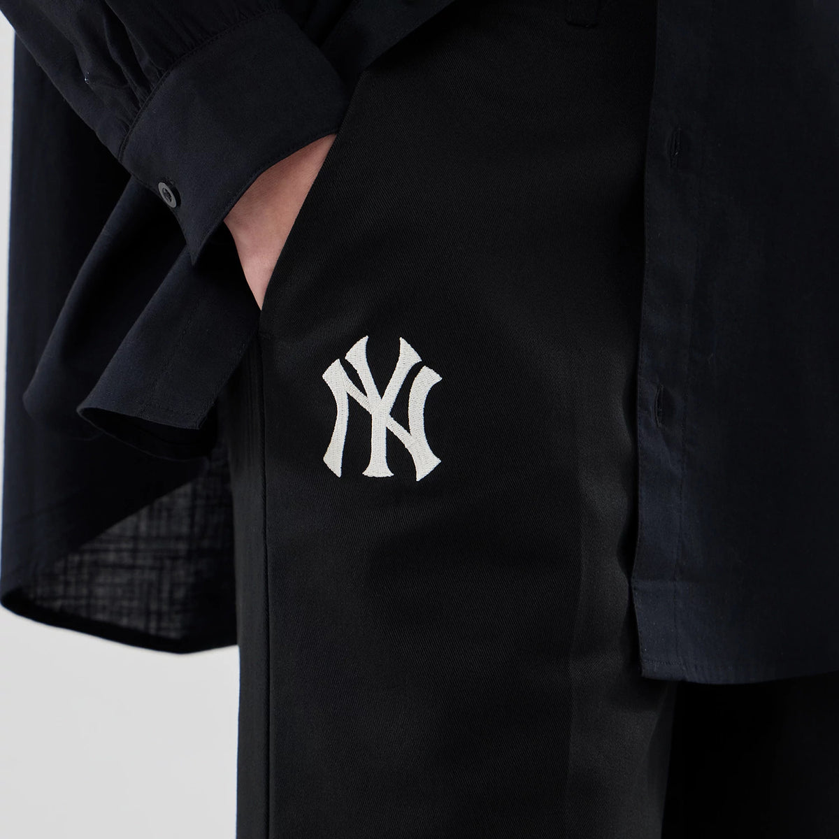 New Era New York Yankees Womens MLB Black Chino Trousers, side view showing embroidered white NY logo on the upper thigh, highlighting the black fabric and tailored fit paired with a matching dark shirt.