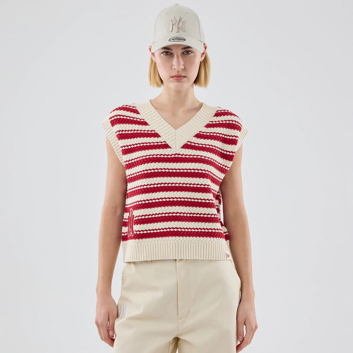 New Era New York Yankees Womens MLB Knit Stripe Dark Red Sleeveless V-neck Sweater, front view on a model styled with a cream-coloured Yankees cap, featuring alternating dark red and cream stripes and a ribbed waistband and armholes.