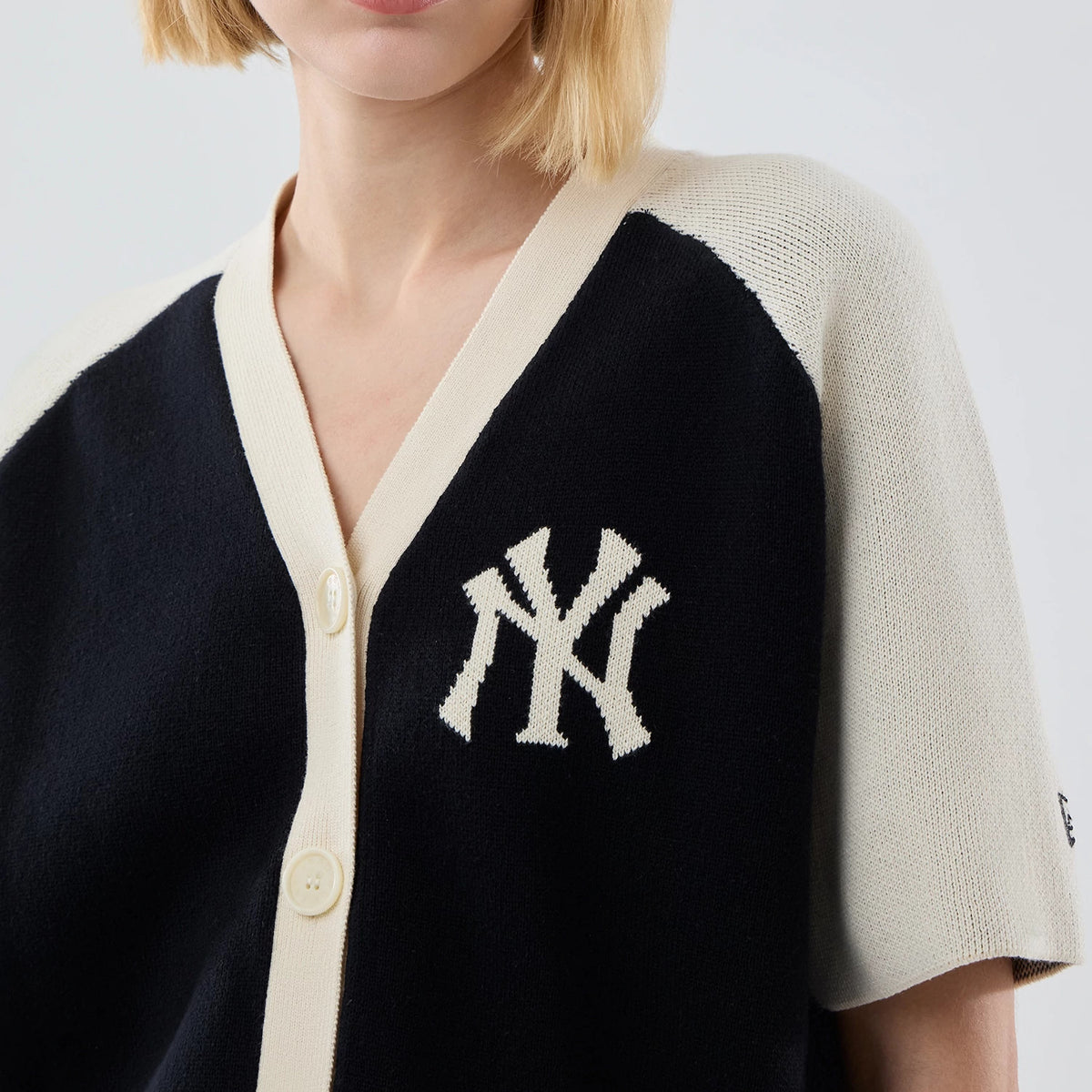New Era New York Yankees Womens MLB Knit Stripe Black Short Sleeve Cardigan, front view on a model showing a white embroidered NY logo on the left chest, cream button fastening, and contrasting cream raglan sleeves.
