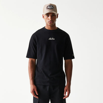 New Era Heritage Script Black T-Shirt, front view on-model showing the embroidered New Era script logo in white on the chest and a small embroidered New Era logo on the left sleeve, styled with a beige New Era cap.
