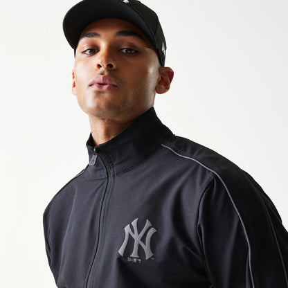 New Era New York Yankees MLB Black Track Jacket, front view on a model highlighting the raised New York Yankees logo on the left chest and a zip closure, paired with a matching black cap featuring an embroidered logo.