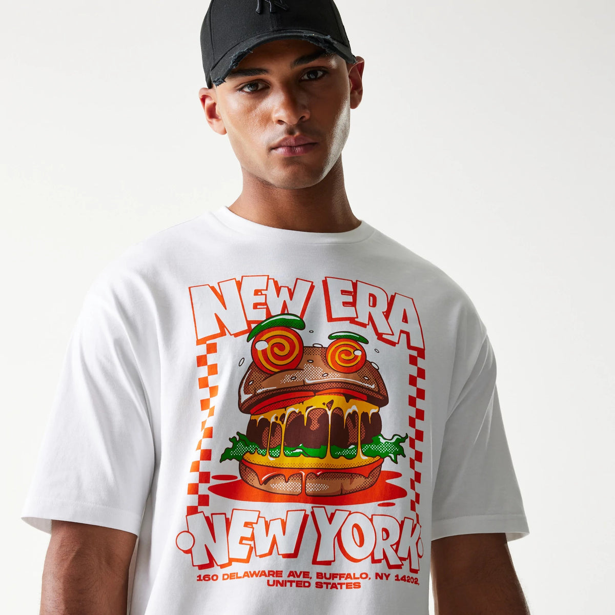 New Era Burger Food Graphic White Oversized T-Shirt, front view on-model showcasing a vivid burger graphic with red New Era and New York text across the chest, complemented by a black cap.