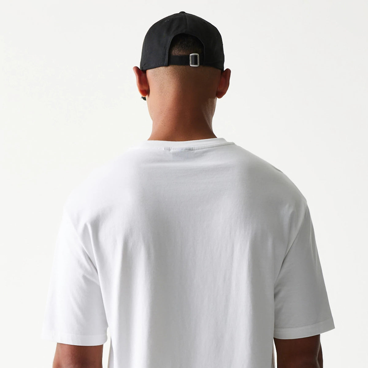 New Era Burger Food Graphic White Oversized T-Shirt, back view on a model wearing a black cap, displaying the plain white fabric and loose fit with a simple round neckline and short sleeves.