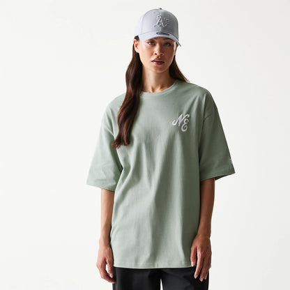 New Era Floral Graphic Pastel Green Oversized T-Shirt, front view showing the pastel green colour with an embroidered NE logo on the left chest, displayed on a model paired with a cap and black trousers.