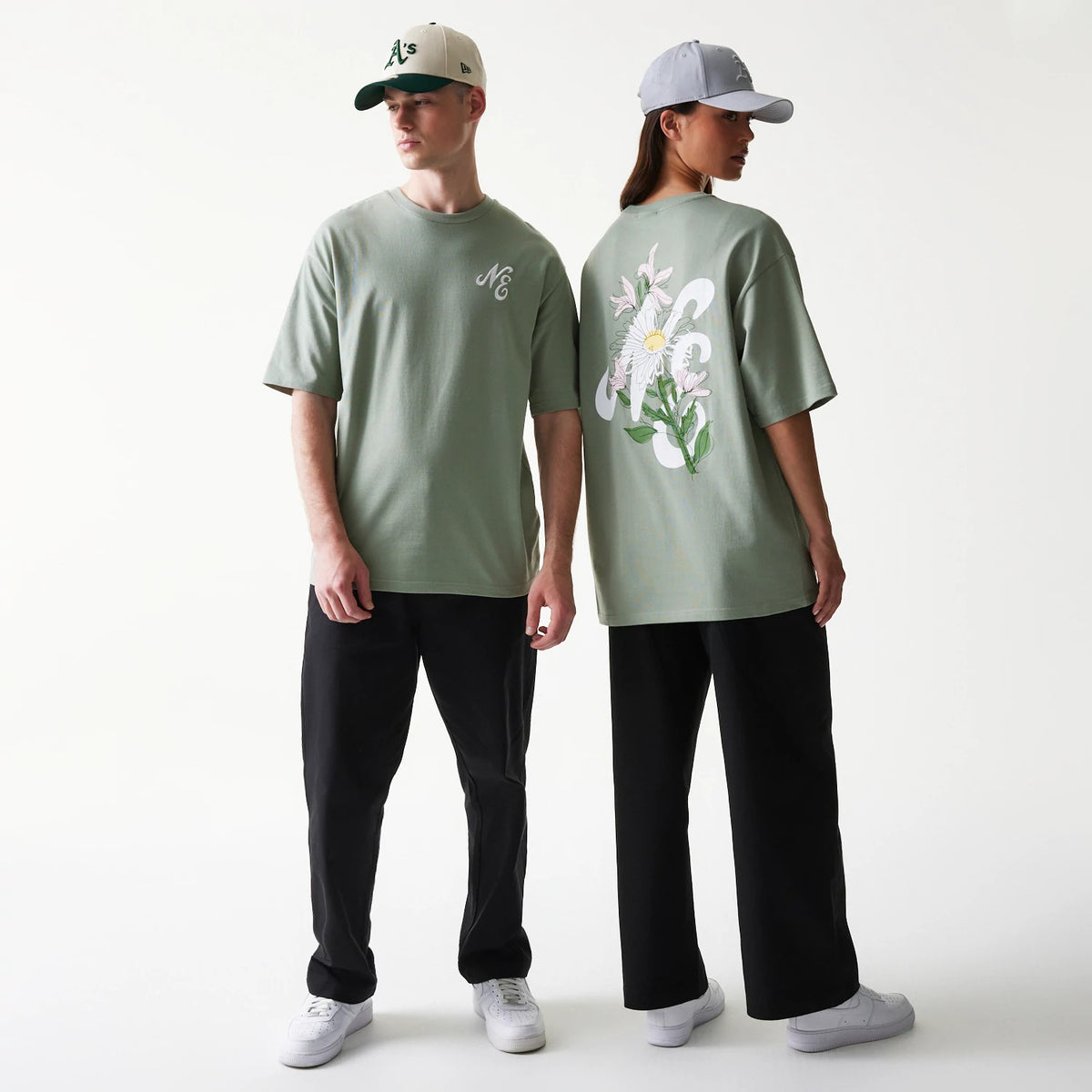 New Era Floral Graphic Pastel Green Oversized T-Shirt, front and back view on models showcasing a pastel green tee with an embroidered logo on the chest and a large floral graphic on the back, styled with black trousers and caps.