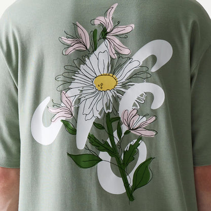 New Era Floral Graphic Pastel Green Oversized T-Shirt, back view showing an intricate design with a large white and yellow daisy surrounded by pink flowers and green leaves, printed across the upper back.