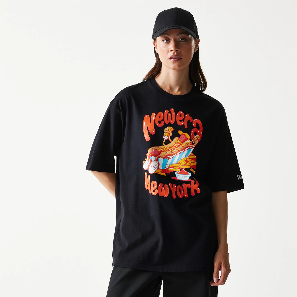 New Era Hotdog Food Graphic Black Oversized T-Shirt, front view on a model showcasing a food graphic featuring hotdogs and fries with New Era New York lettering in red, and an embroidered New Era logo on the left sleeve.