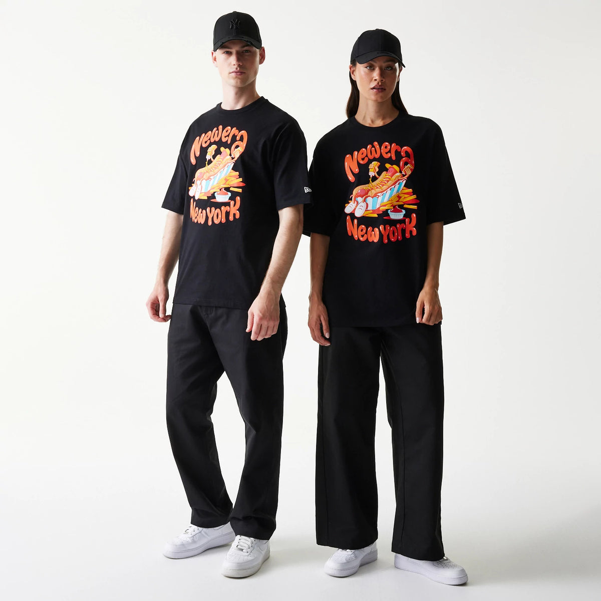 New Era Hotdog Food Graphic Black Oversized T-Shirt, front view on-model showing a graphic of a hotdog with colourful toppings, 'New Era New York' lettering, and an embroidered New Era logo on the sleeve.
