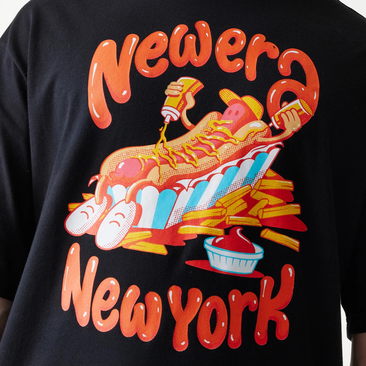 New Era Hotdog Food Graphic Black Oversized T-Shirt, back view showing a graphic of a hotdog with arms, surrounded by fries and sauce, above orange New Era New York lettering on the black fabric.