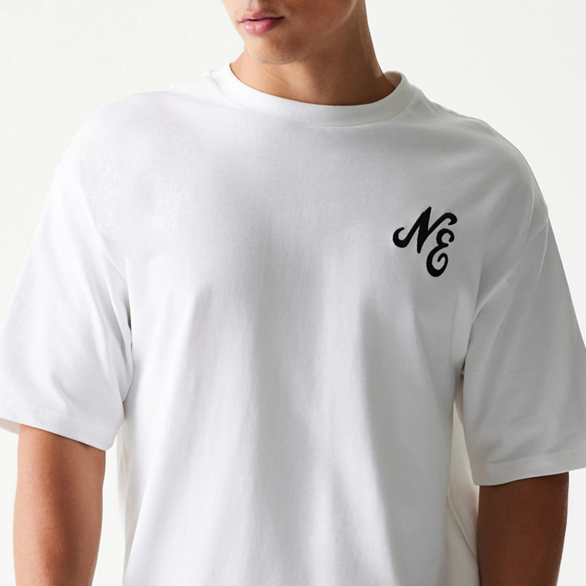 New Era Floral Graphic White Oversized T-Shirt, front view on-model showing a black embroidered NE logo on the left chest, emphasising the loose fit and short sleeves against the plain white fabric.