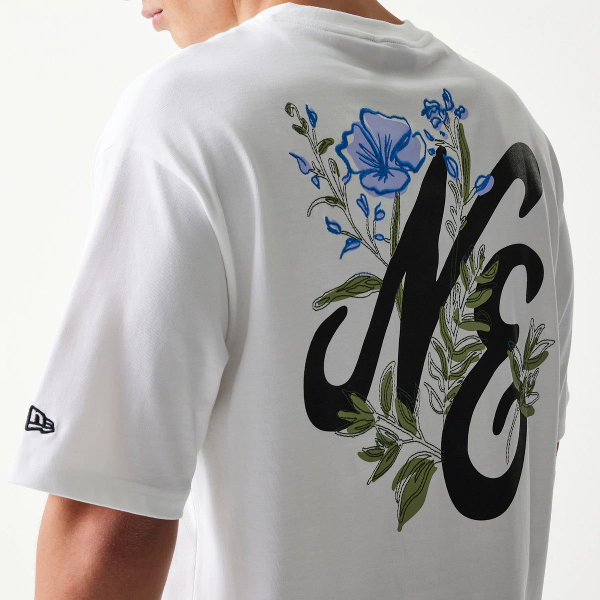 New Era Floral Graphic White Oversized T-Shirt, three-quarter view showing the large black NE lettering on the back surrounded by blue and green floral graphics, with a small embroidered New Era logo on the sleeve.