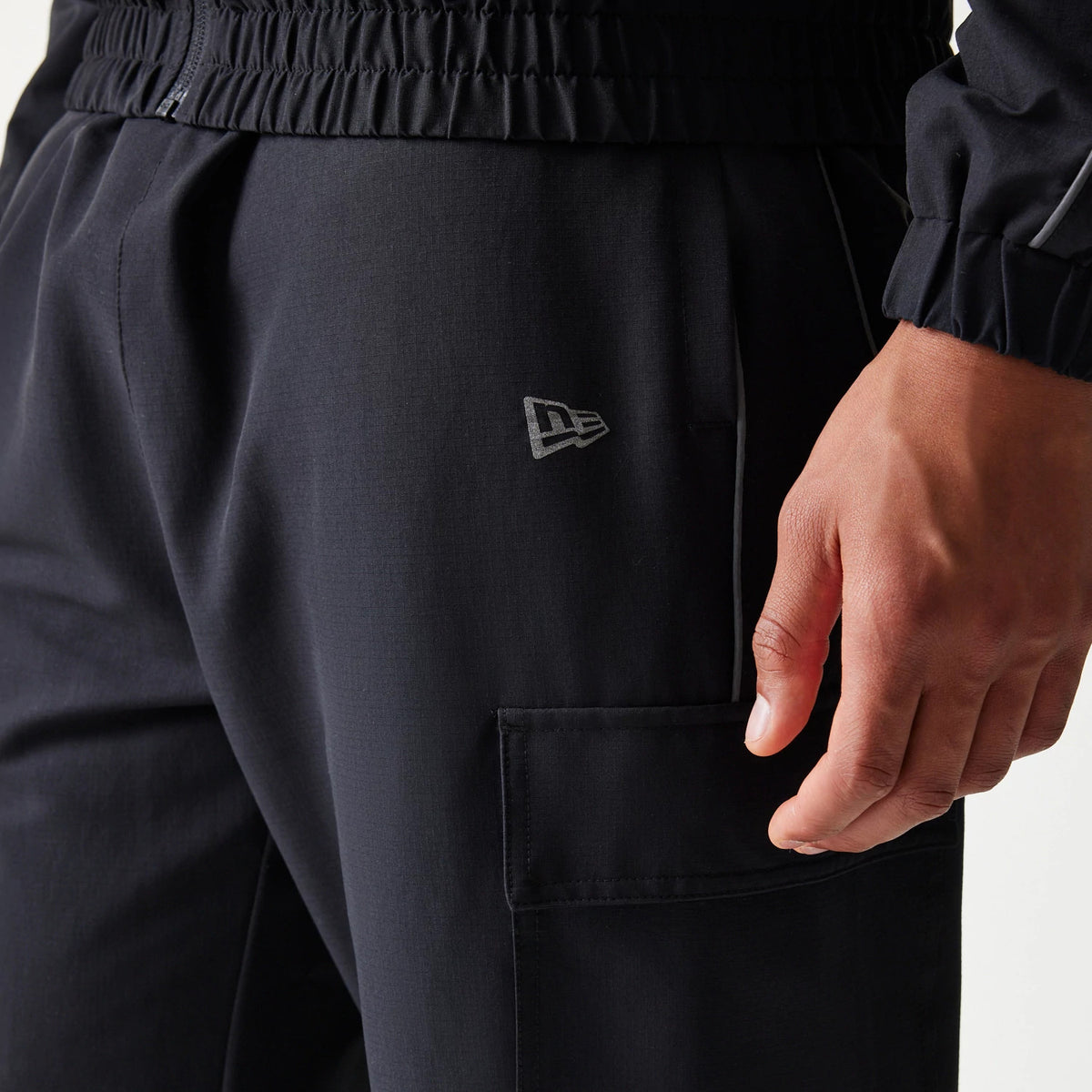 New Era New York Yankees MLB Utility Black Straight Leg Cargo Joggers, side view showing the grey New Era flag logo on the left thigh, large cargo pocket with a flap, and an elastic waistband with stitching details.