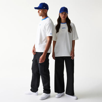 New Era Script White Oversized T-Shirt, front view on two models paired with blue caps, featuring the embroidered New Era script logo centred on the chest and a contrasting blue neckline accentuating the white fabric.