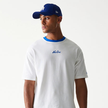 New Era Script White Oversized T-Shirt, front view on-model showing the blue embroidered New Era script centrally placed on the chest, paired with a blue cap, and a blue neck trim adding contrast to the white fabric.