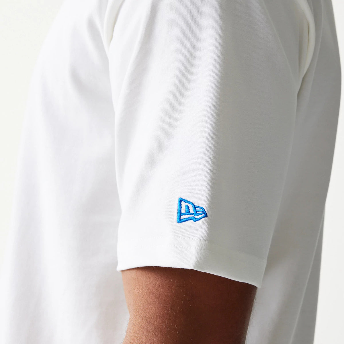 New Era Script White Oversized T-Shirt, side view showing the short sleeve with a blue embroidered New Era logo near the hem, highlighting the classic white design on a model's upper arm.