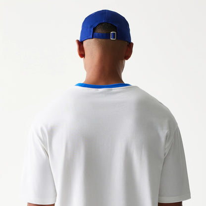 New Era Script White Oversized T-Shirt, back view on-model showing a plain white back with a contrasting blue collar, styled with a blue cap featuring an adjustable strap at the back.
