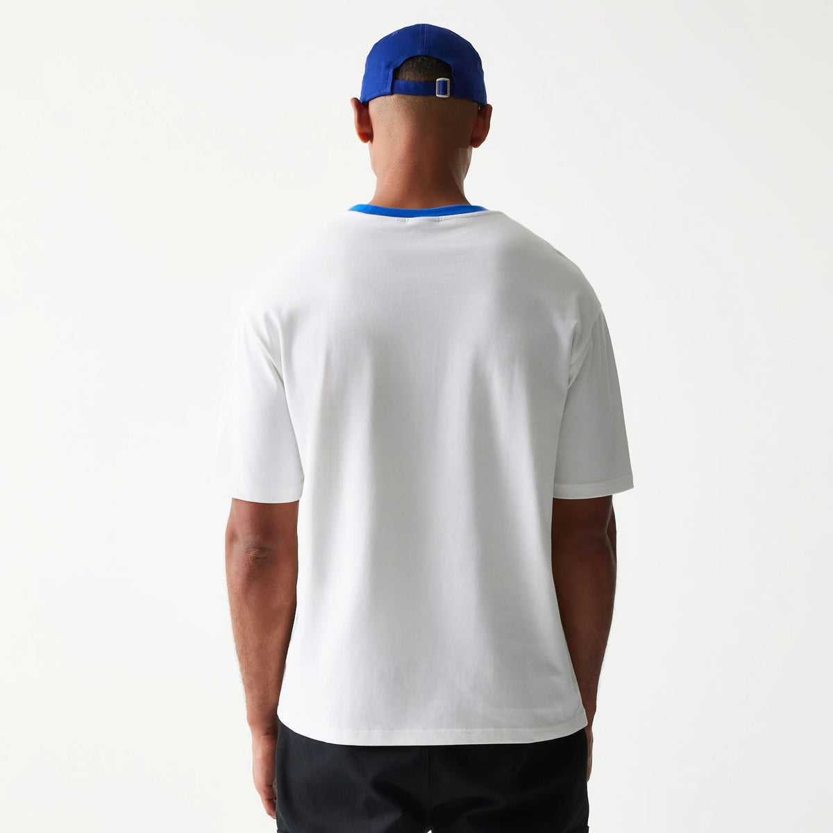 New Era Script White Oversized T-Shirt, back view on-model showcasing a plain white back with oversized fit, paired with a blue cap and contrasting blue trim at the collar for a pop of colour.